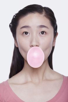 Young playful woman blowing a bubble out of bubble gum, studio shot 