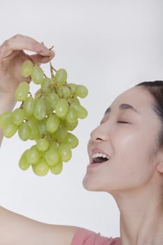 Young woman enjoying a bunch of grapes raised above her head, studio shot