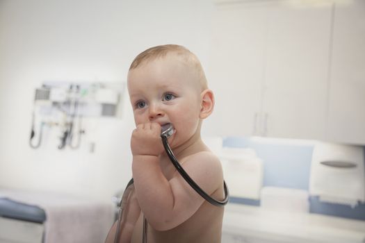 Curious baby holding and biting a stethoscope in the doctors office