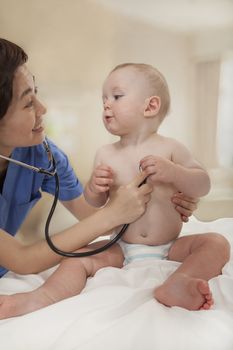 Smiling doctor checking a baby's heart beat with a stethoscope  in the doctors office