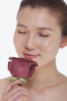 Beautiful young woman with eyes closed smelling a red rose, studio shot