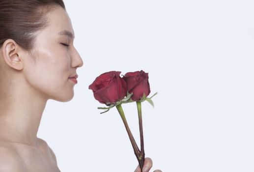 Beautiful young woman with eyes closed smelling a red rose, studio shot