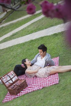 Young happy couple lying on a blanket together while having a picnic in the park, blossoms in the foreground