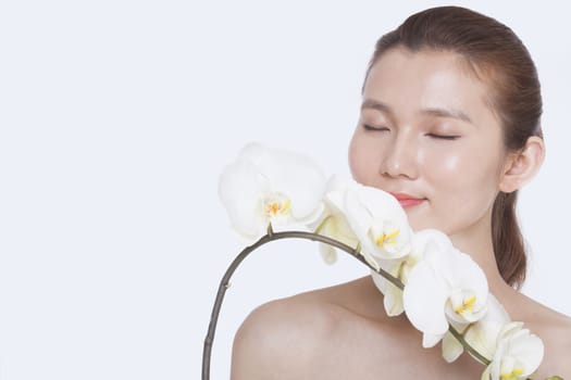 Shirtless young woman with eyes closed smelling a bunch of beautiful white flowers, studio shot