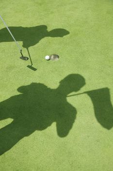 Shadows of two golfers hitting the ball on the golf course, ball in the hole