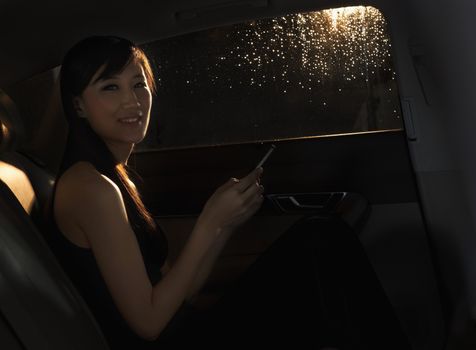 Young woman sitting in the car, on her phone, and looking at the camera on a rainy night in Beijing