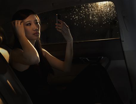 Young woman sitting in her car and checking her hair in the phone before going out on a rainy night in Beijing