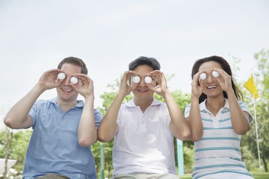 Three smiling friends in a row holding up golf balls in front of their eyes