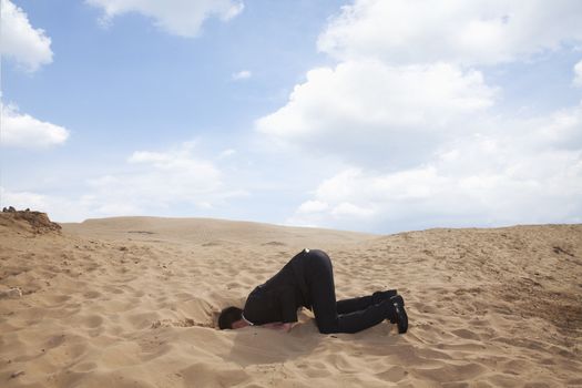 Young businessman kneeling with his head in a hole in the sand