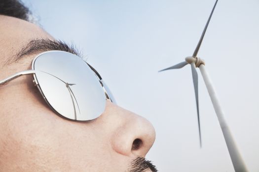Close up of young mans face with the reflection of the wind turbine in his sunglasses