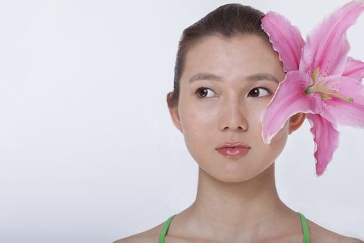 Portrait of young beautiful woman with a large pink flower tucked behind her ear, studio shot