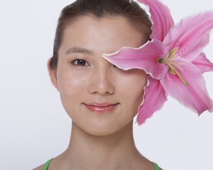 Portrait of young, smiling, beautiful woman with a large pink flower tucked behind her ear, studio shot