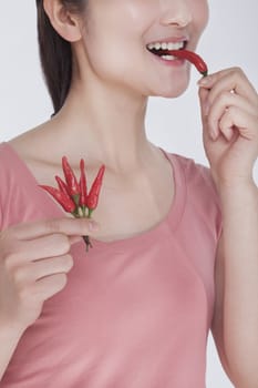 Young woman in pink shirt eating a  chili pepper, studio shot, half face showing