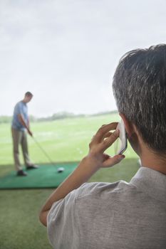 Rear view of man on the phone while another man plays golf in the background