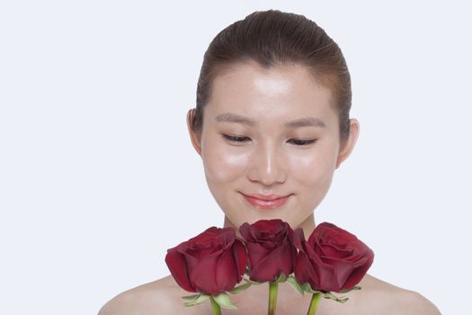 Young, beautiful, smiling woman looking down at a bunch of red roses, studio shot