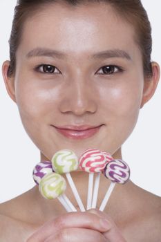 Smiling young woman looking into camera and holding up colorful lollipops, studio shot