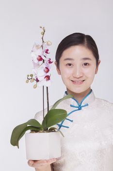 Portrait of smiling young woman holding a beautiful white flower in a flower pot, studio shot