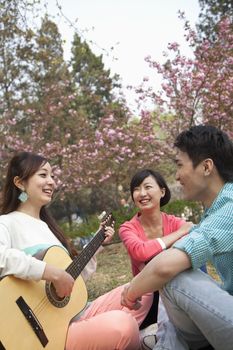Young happy friends hanging out in the park in springtime, playing guitar