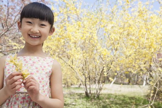 Portrait of smiling girl holding a yellow flower in the park in springtime