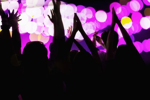 Audience watching a rock show, hands in the air, rear view, stage lights