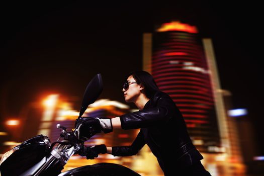 Beautiful young woman riding motorcycle in sunglasses through the city streets at night