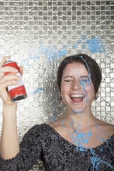 Young woman laughing and spraying party string over herself