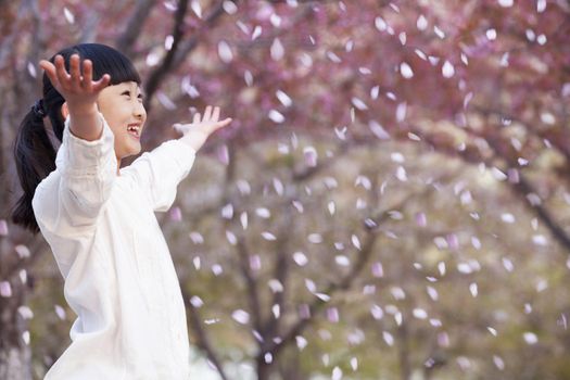 Happy young girl throwing cherry blossom petals in the air outside in a park in springtime