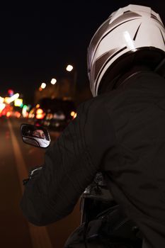 Young man riding a motorcycle through the streets of Beijing at night, rear view