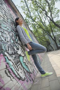 Young woman leaning and hanging out by a wall covered in graffiti