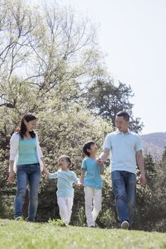 Family holding hands, walking in park.