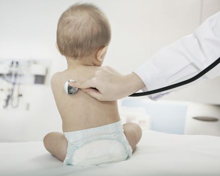 Baby sitting in the doctors office with the doctors hand checking heart beat with a stethoscope