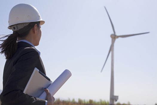 Young female engineer holding blueprints and checking wind turbines on site, 