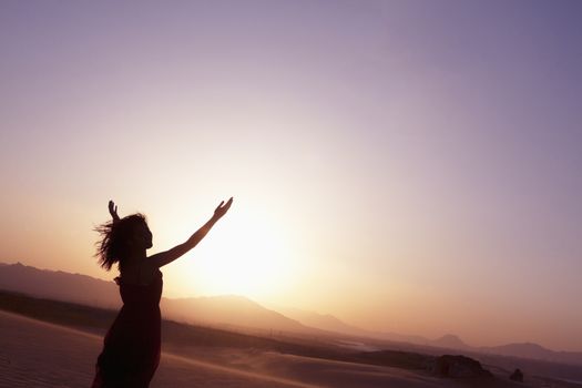 Serene young woman with arms outstretched doing yoga in the desert in China, Silhouette