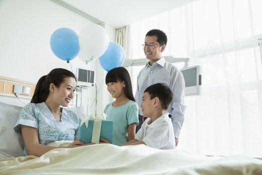 Father and children visiting their mother in the hospital, giving present and balloons