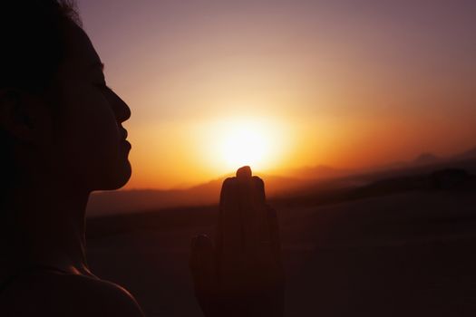 Serene young woman with hands together in prayer pose  in the desert in China, silhouette, sun setting