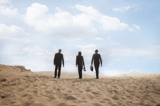 Three young business people walking through the desert, rear view, distant