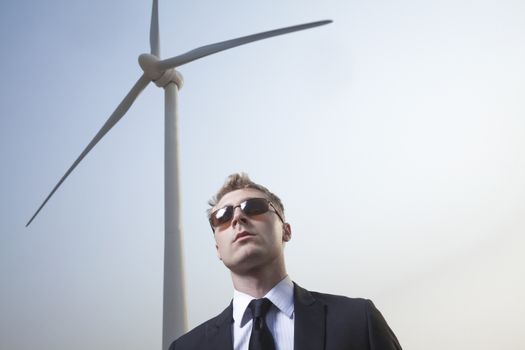 Portrait of serious young businessman in sunglasses standing by a wind turbine