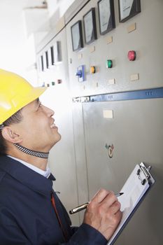 Smiling worker holding clipboard and checking controls in a gas plant, Beijing, China