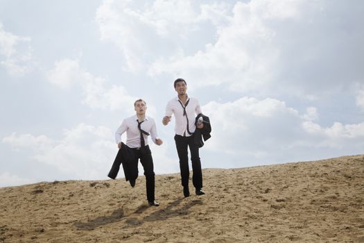 Two young businessmen running and exhausted in the desert, holding jackets
