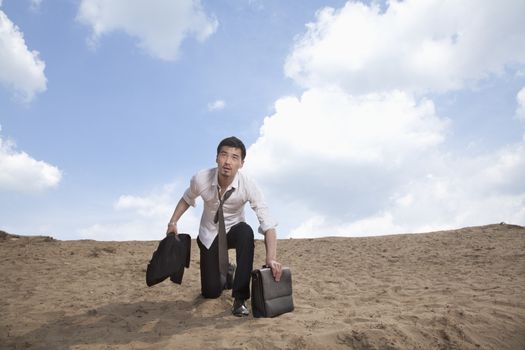 Young businessman kneeling in the desert and holding a briefcase, exhausted