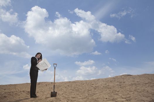 Young businesswoman looking at a blueprint next to a shovel in the middle of the desert