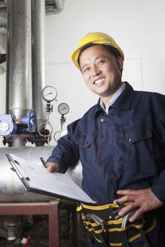 Portrait of smiling worker with a clipboard checking the oil pipeline equipment in a gas plant, Beijing, China