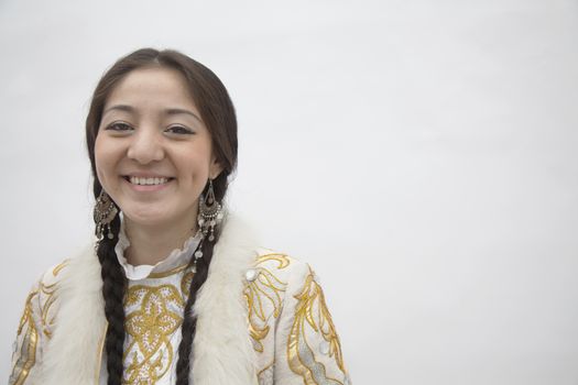 Portrait of young smiling woman with braids in traditional clothing from Kazakhstan, studio shot