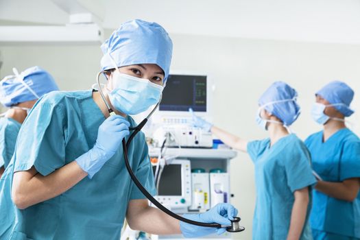 Team of surgeons in the operating room, female surgeon holding stethoscope and looking at camera