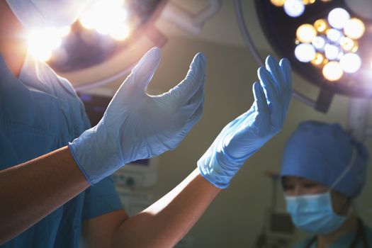 Midsection view of hands in surgical gloves and surgical lights in the operating room 