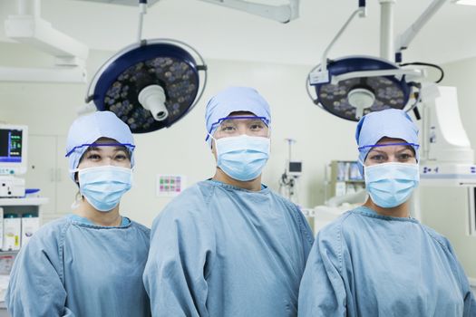 Portrait of three surgeons in a row wearing surgical masks in the operating room, looking at camera