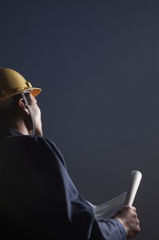 Young male engineer in a hardhat holding a blueprint at dusk, rear view