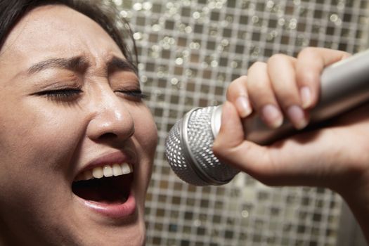 Close-up of young woman singing into a microphone at karaoke