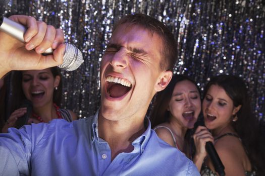 Young man singing into a microphone at karaoke, friends singing in the background