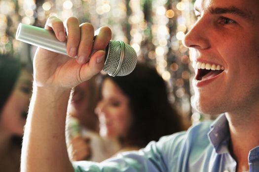 Close- up of young man holding a microphone and singing at karaoke, friends singing in the background